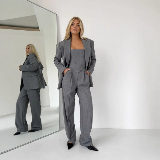 Woman in a gray suit standing in front of a mirror on a white background