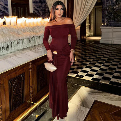 Woman in a burgundy off-shoulder dress standing in an elegant interior setting with candles and marble.