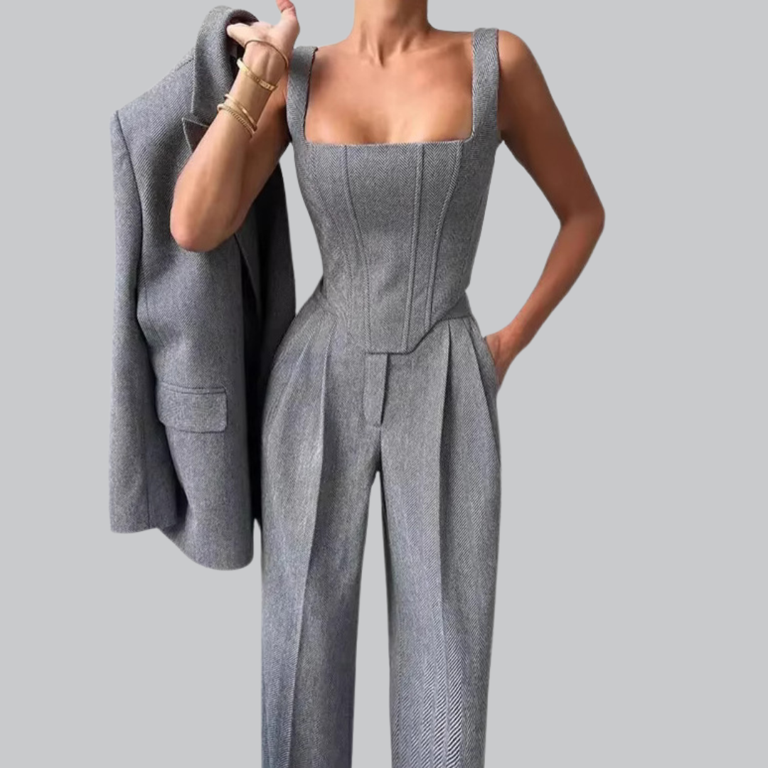 Person wearing a gray jumpsuit holding a gray blazer against a plain background