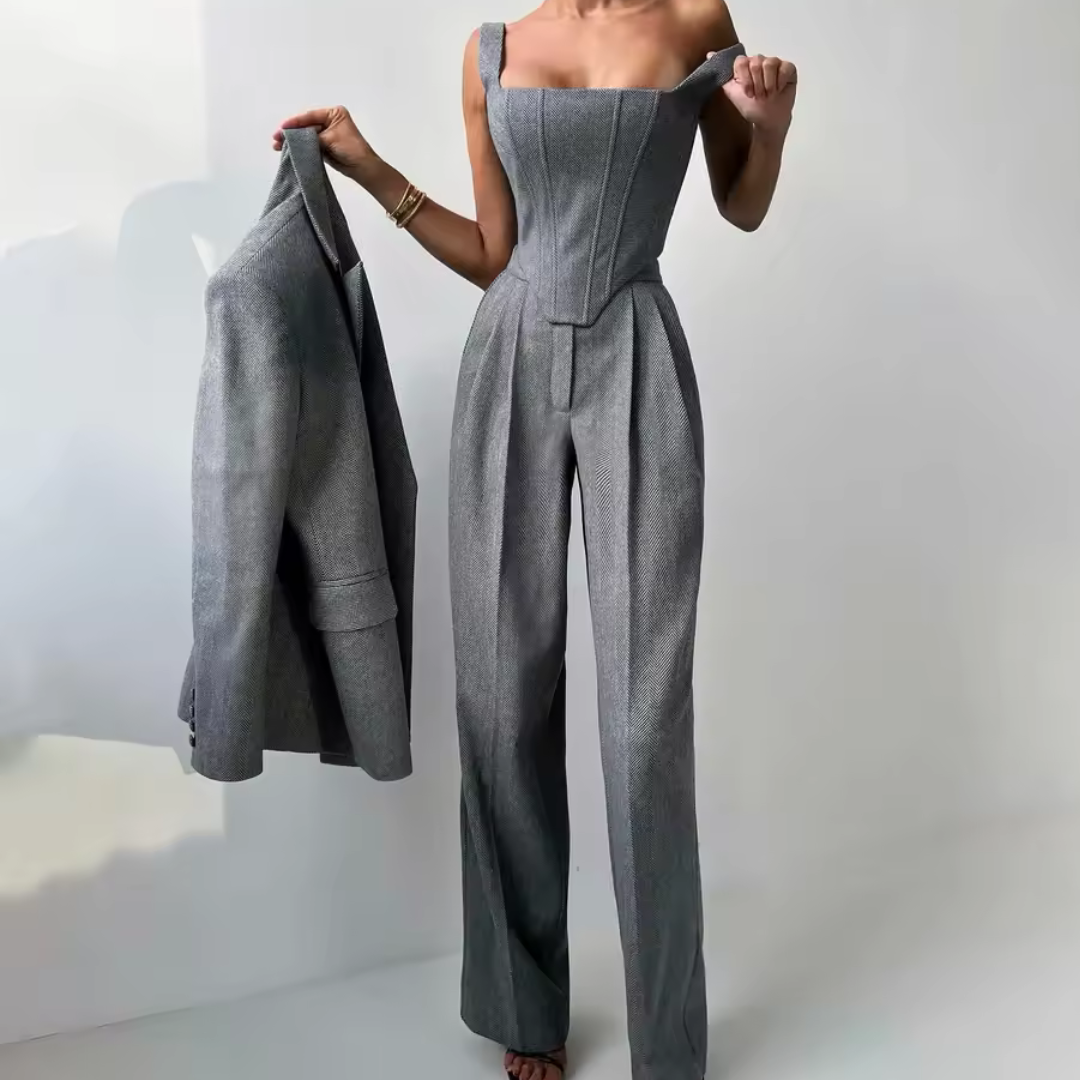 Person wearing a gray jumpsuit holding a matching jacket against a white background