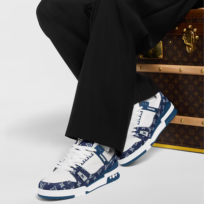 White sneakers with blue pattern worn by a person sitting next to a Louis Vuitton suitcase.