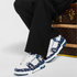 White sneakers with blue pattern worn by a person sitting next to a Louis Vuitton suitcase.